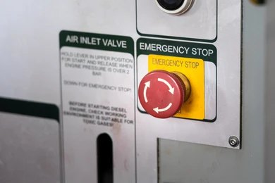 A close-up of a red emergency stop button on an industrial machine's control panel.