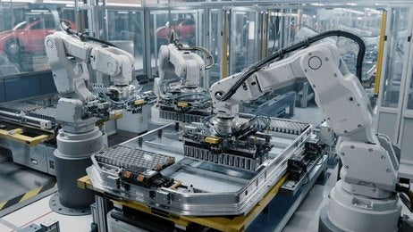 Three robotic arms working on an electric vehicle battery pack on a modern factory assembly line.