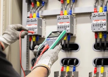 An electrician in protective gloves using a multimeter to test industrial circuit breakers.