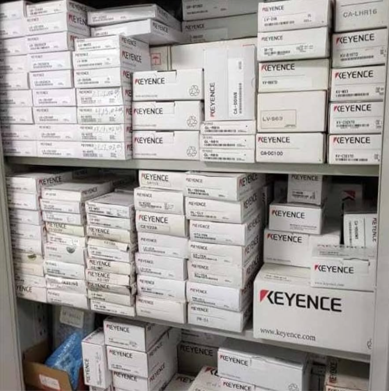 Keyence laser sensor boxes stacked on shelves, showing various product models for industrial applications.