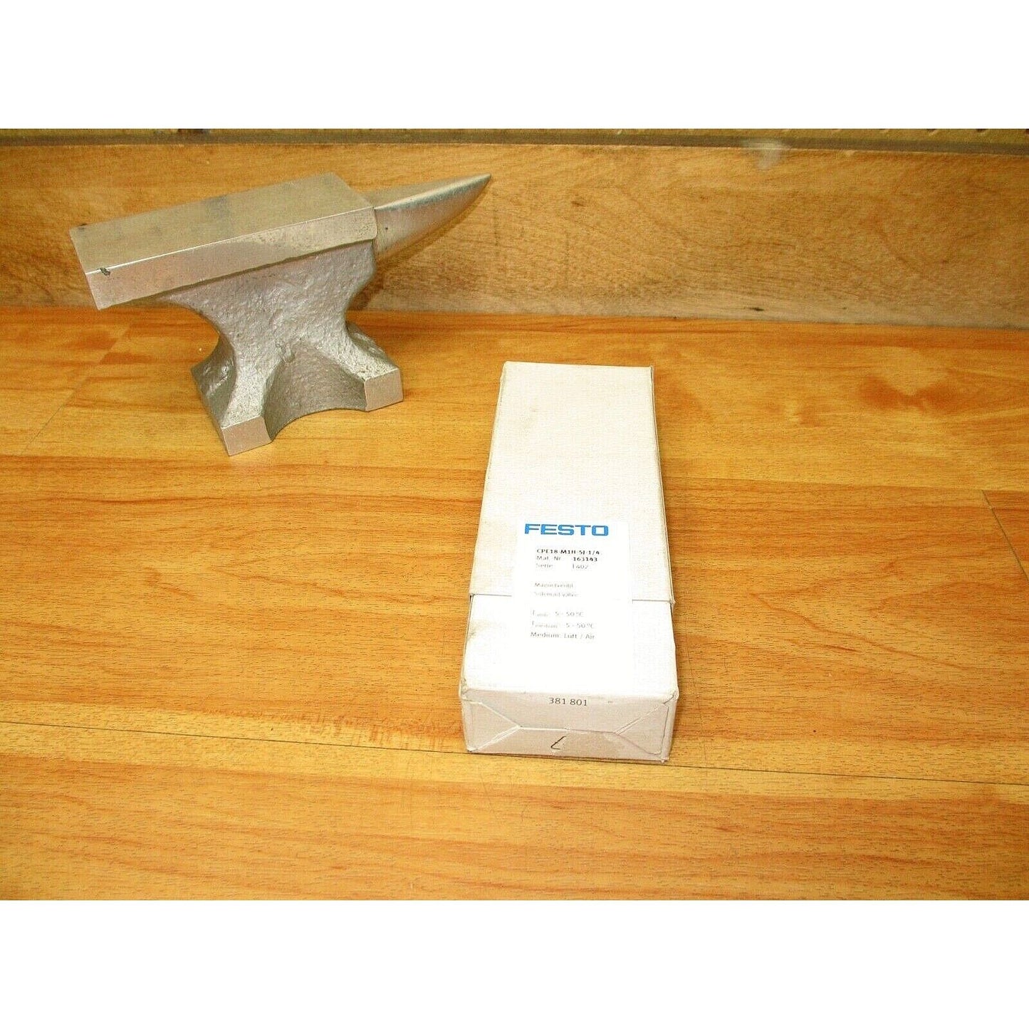 FESTO CPE18-M1H-5J-1/4 Solenoid Valve packaging with a metal anvil on a wooden surface.