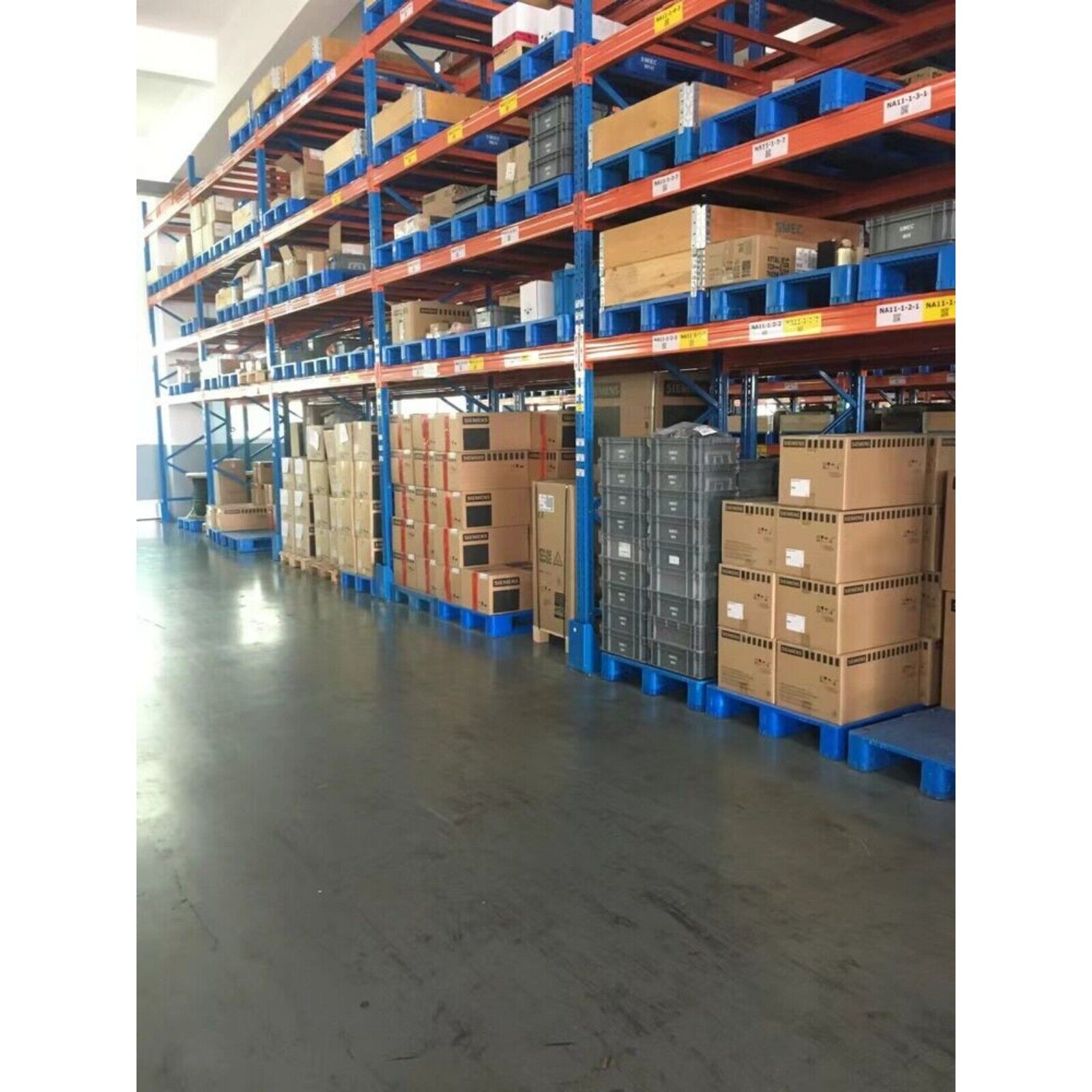 Industrial automation parts warehouse with stocked shelves and packaged products, featuring Siemens branding on boxes.