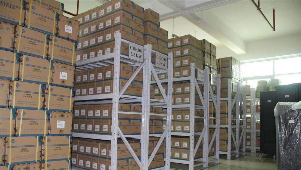 Warehouse storage of CDE300 products, stacked boxes on metal shelving. 2.2kW and 3.7kW models.