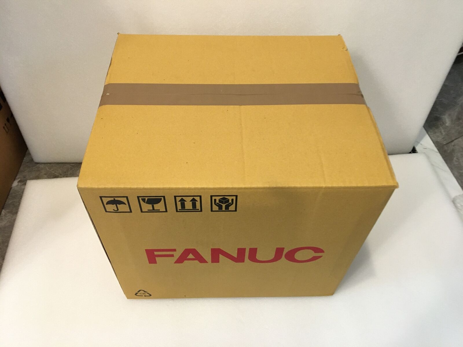 FANUC servo amplifier product packaging, brown cardboard box with brand logo and shipping symbols, new servo drive