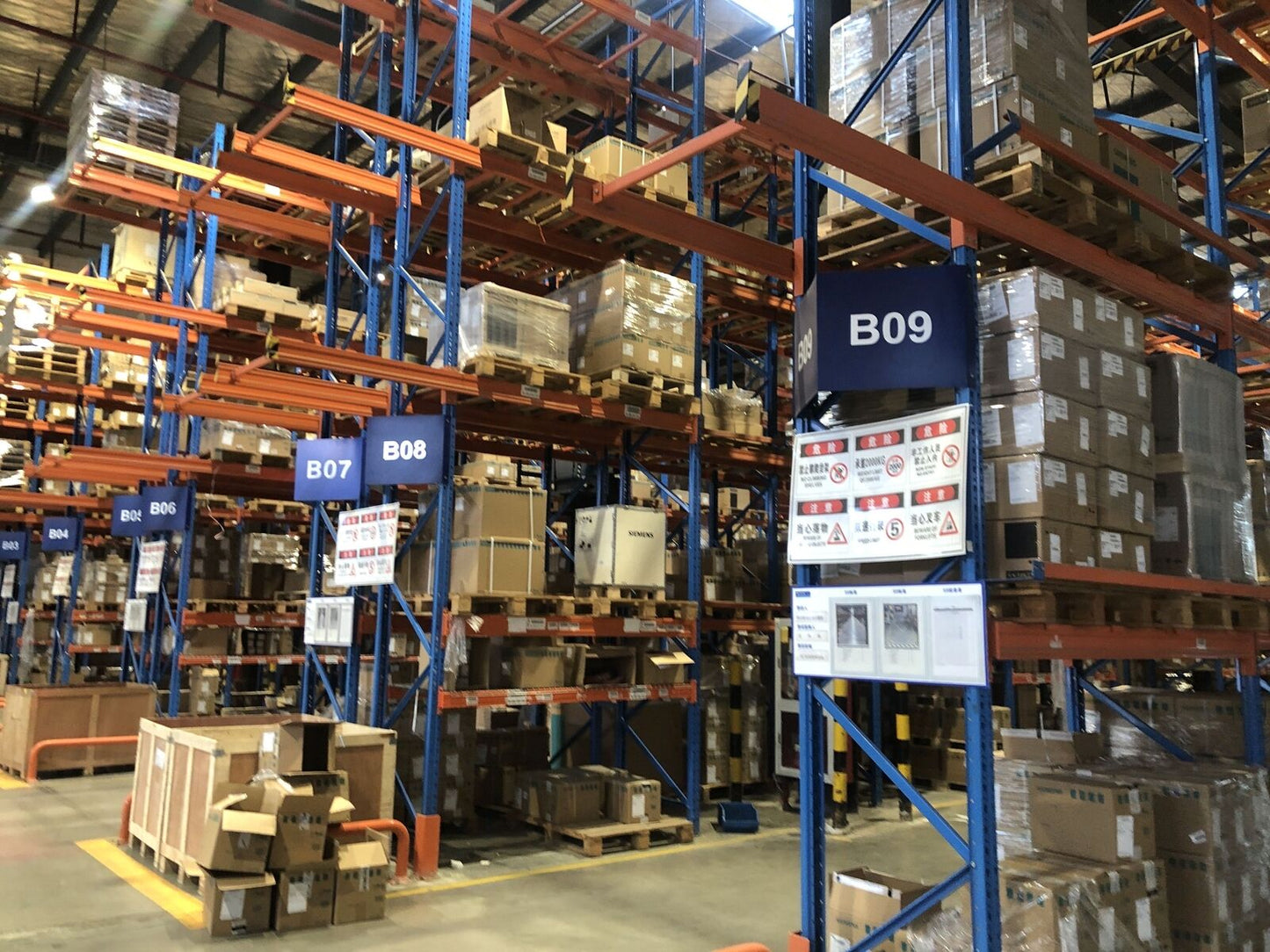 Warehouse storage of Mitsubishi FR-E740-2.2K-CHT inverters and industrial automation parts, safety signage visible.